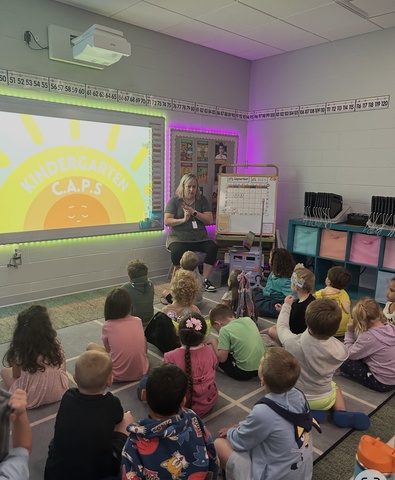 Someone talking to a class full of kids and all the kids are watching and listening. 