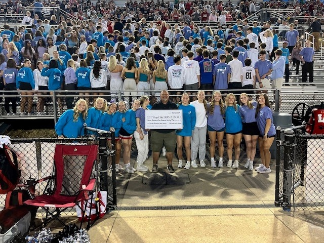 A crowd of people standing at a football field holding a check 