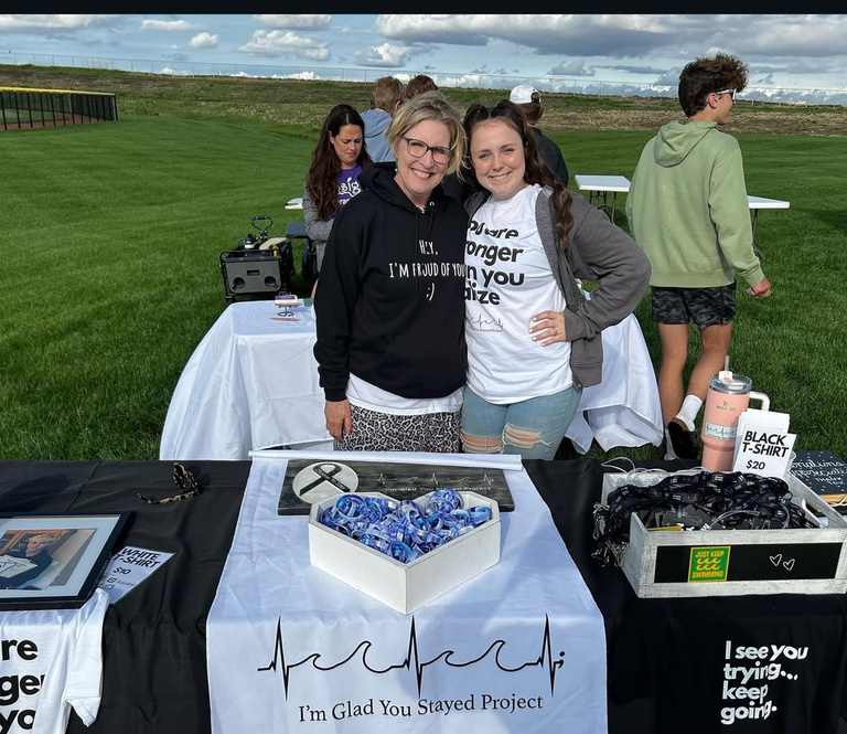 Two people outside standing behind a table looking into the camera smiling.