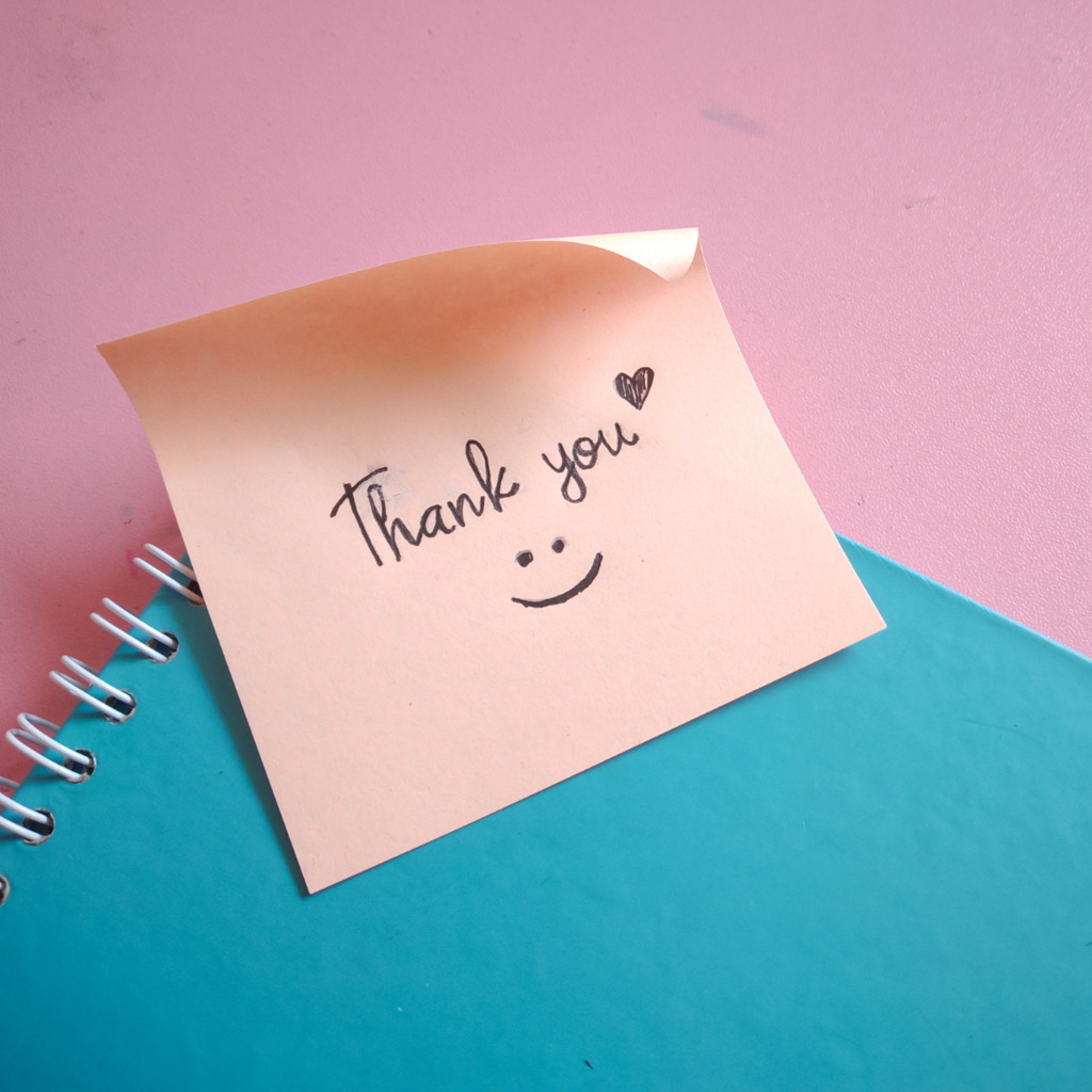 "Thank you" written on a pink post-it note on a blue notebook