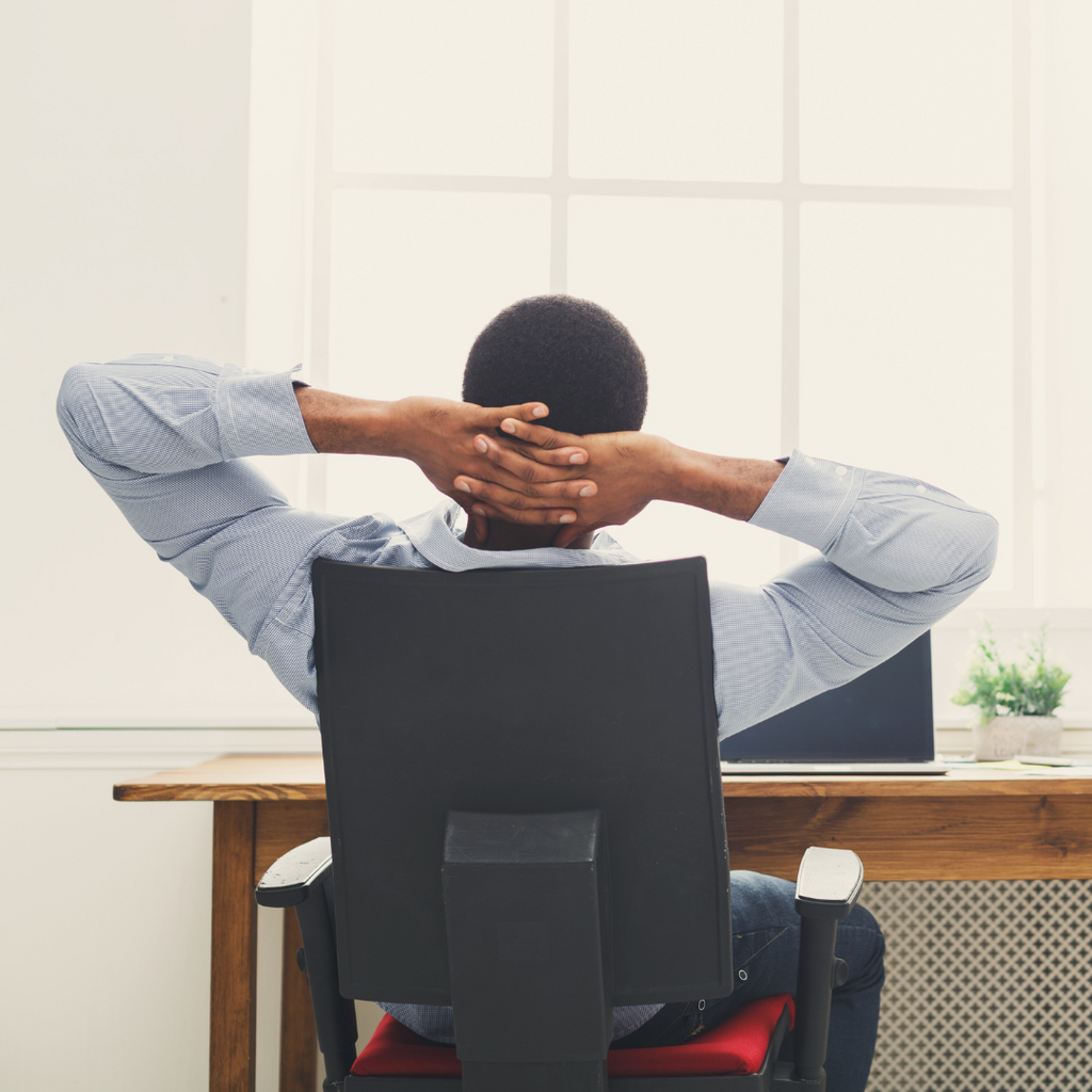 Man sitting in an office chair facing a window and hands behind head