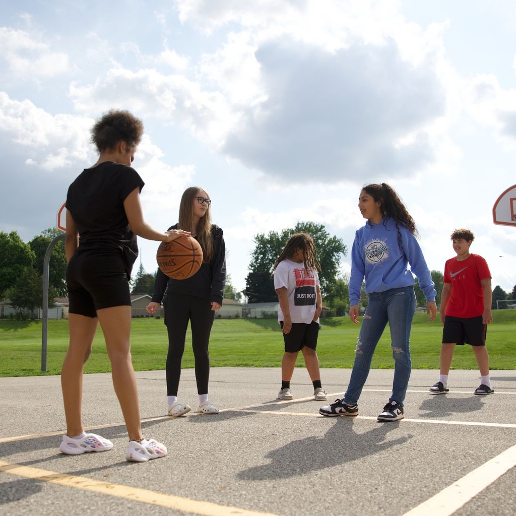 A group of kids playing basketball on a playground with clouds in the sky