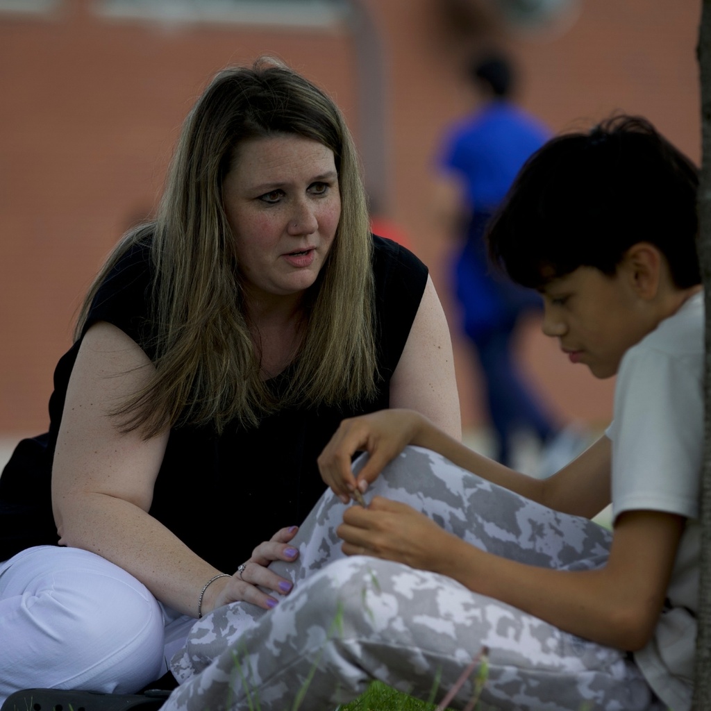 teacher sitting with student outside by a tree