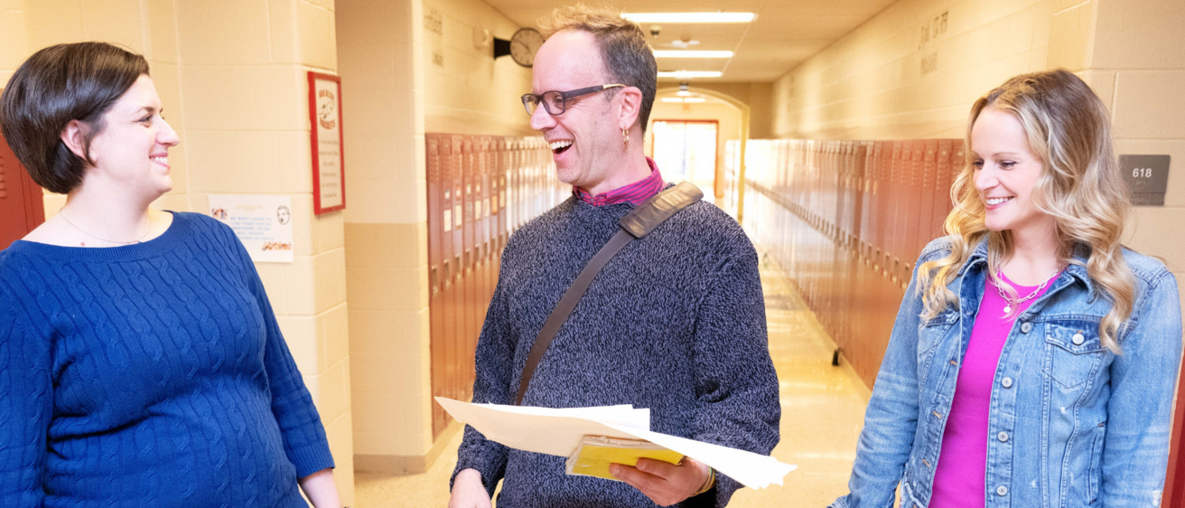 three adults talking in school hallway