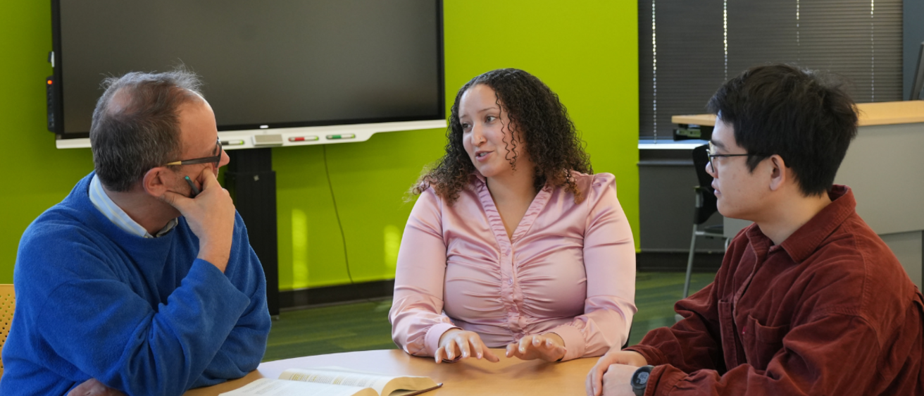 Faculty member talking with two students sitting a table