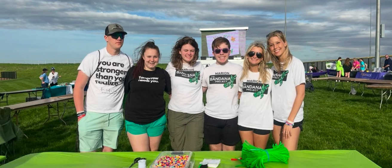 Six people standing outside, behind a table, looking into the camera smiling. 