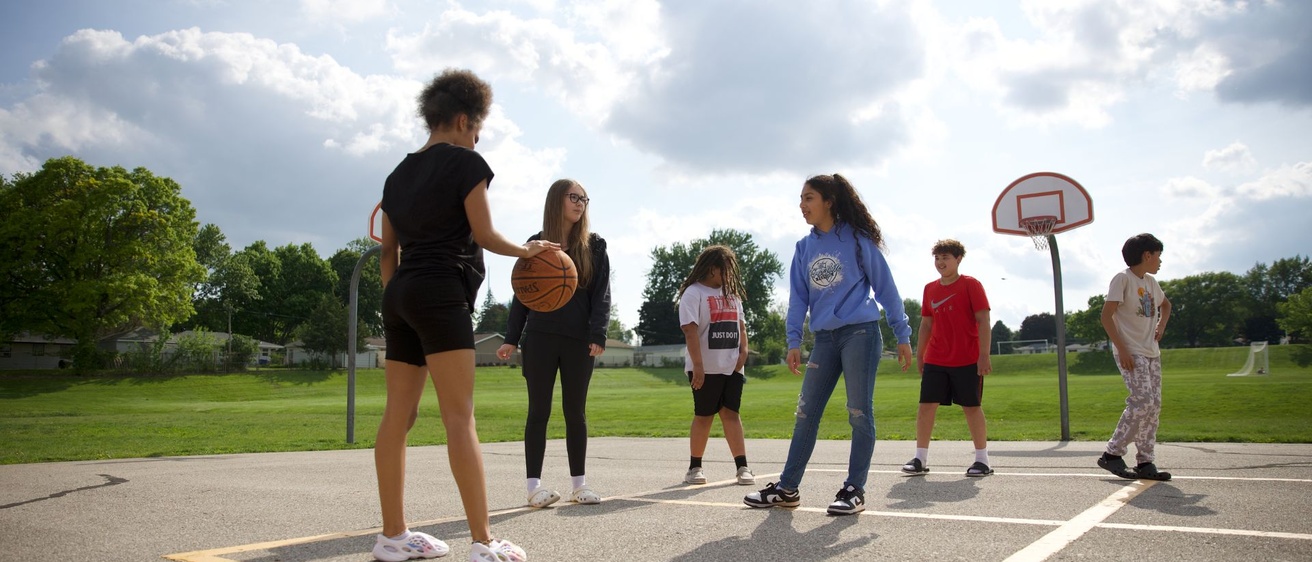 A group of kids playing basketball on a playground with clouds in the sky