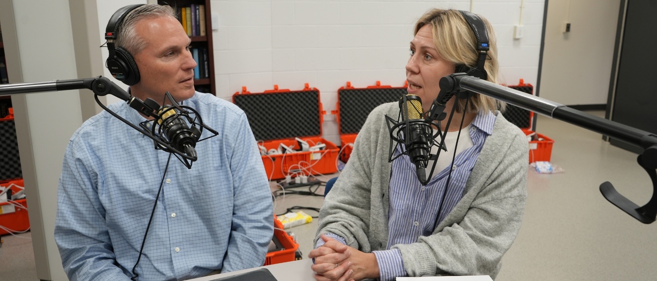 Two podcast co-hosts talking with each other, each with a mic and headset