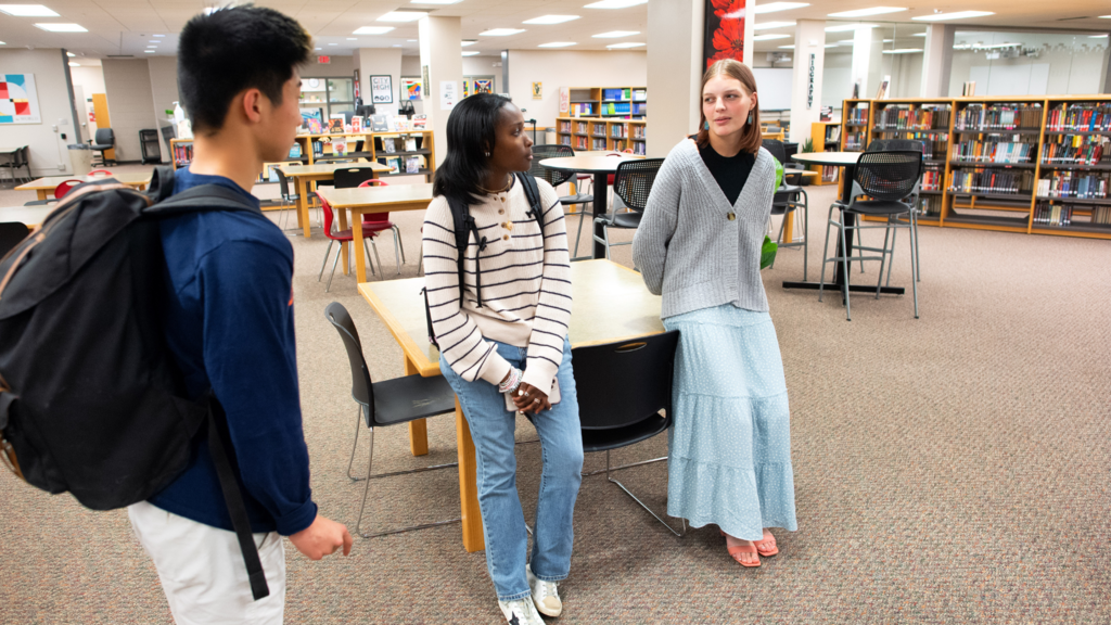 three students standing in library