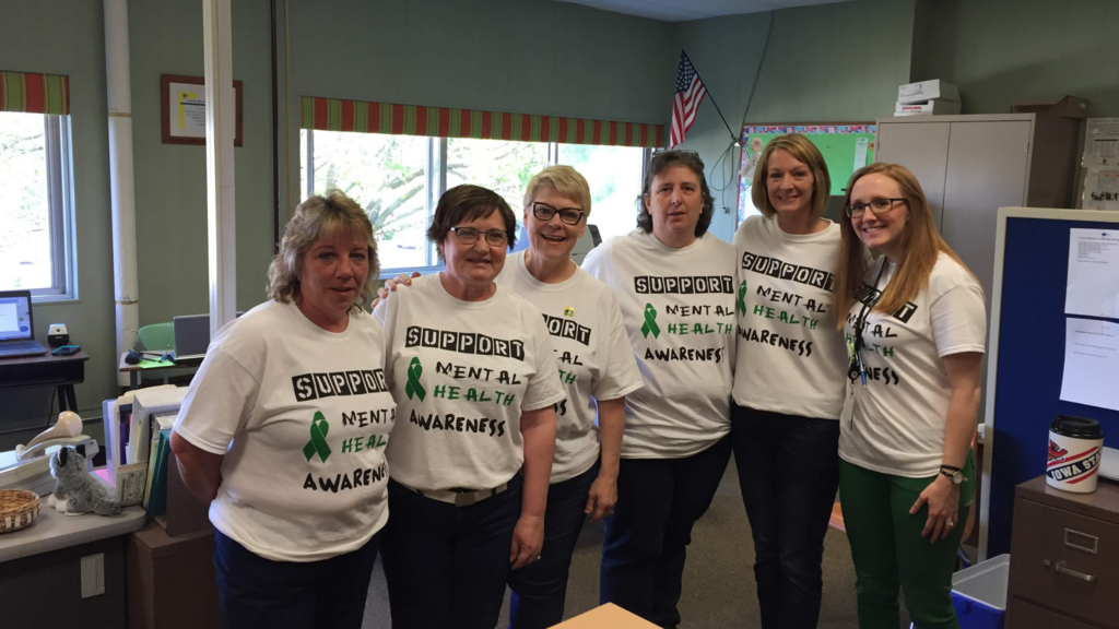 A group of five educators wearing t-shirts that say "Supporting Mental Health Awareness"