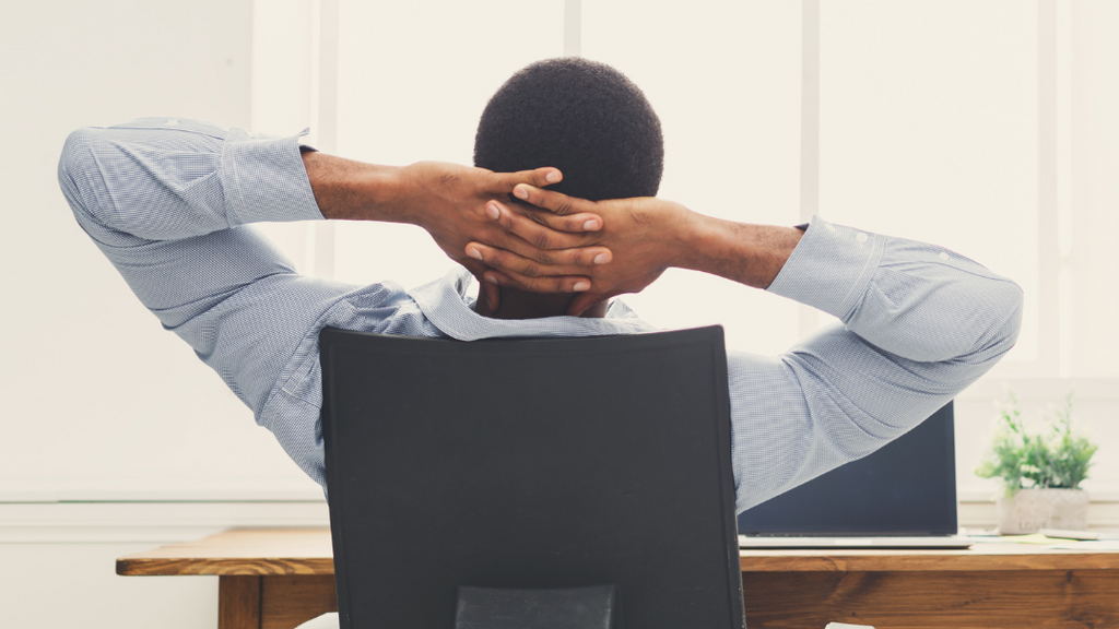 Man sitting in an office chair facing a window and hands behind head