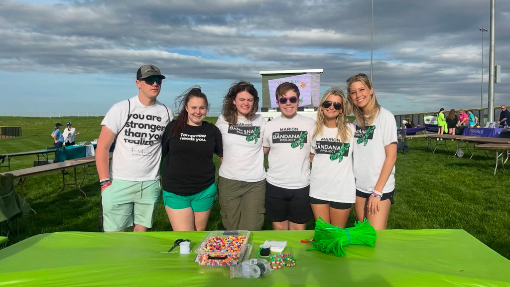 Six people standing outside, behind a table, looking into the camera smiling. 