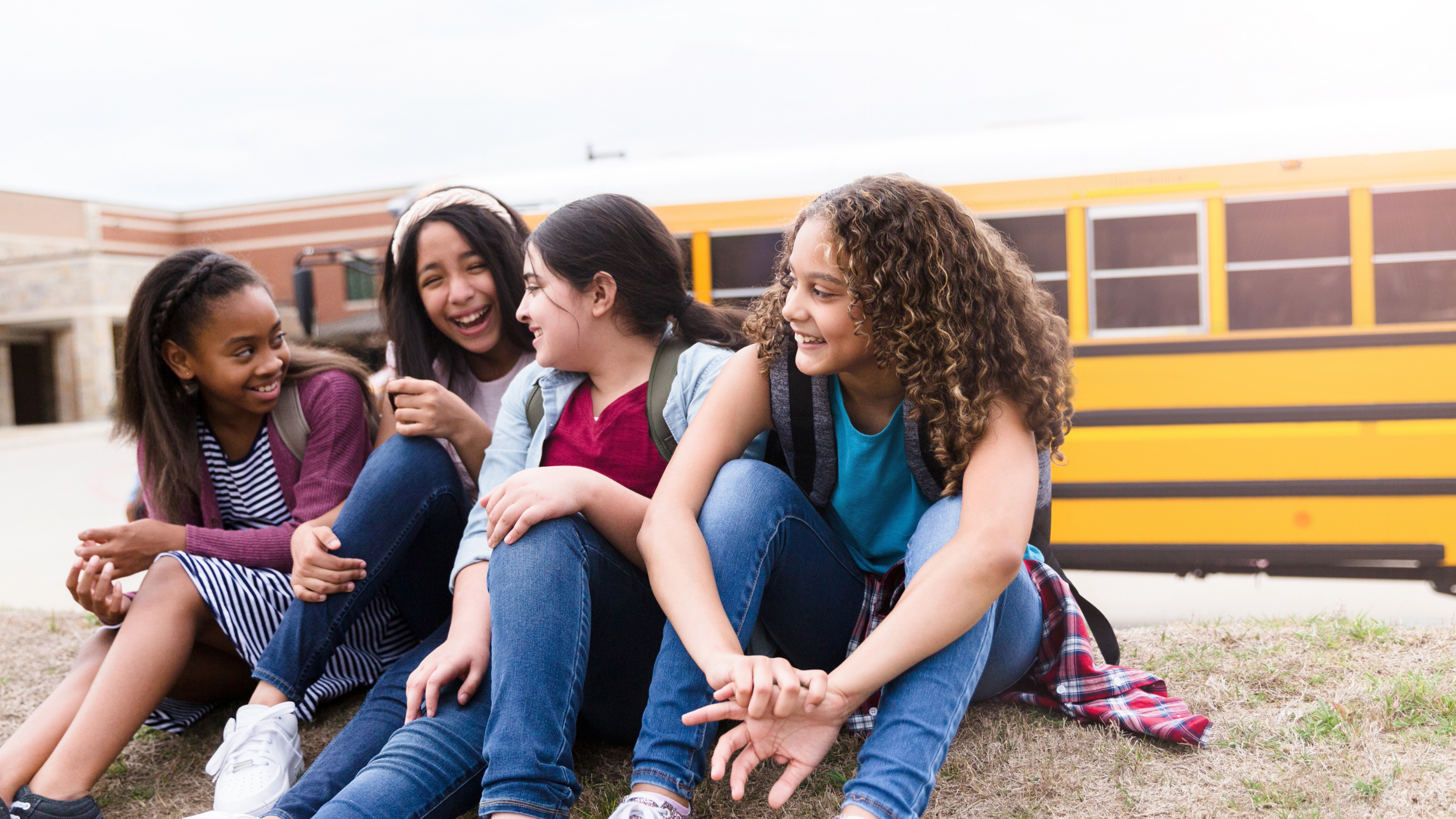 Four middle school students sitting by bus